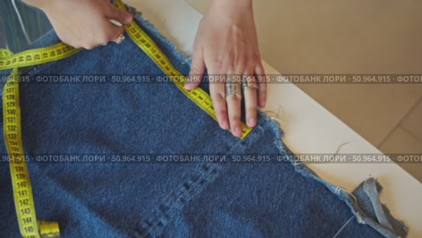 Hands are adjusting measuring tape on the denim material, marking it with a piece of chalk. Стоковое видео, видеограф Strunov David / Фотобанк Лори