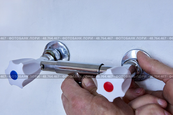 Hands are installing new two handle faucet onto wall outlets, plumber tightens metal fixture with white handles to exposed threaded connectors. Стоковое фото, фотограф Владимир Григорьев / Фотобанк Лори