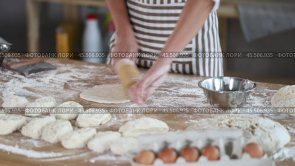Hands of skilled female baker in striped apron rolling out soft dough on flour-dusted wooden table in bakery. Cropped shot. Стоковое видео, видеограф Яков Филимонов / Фотобанк Лори