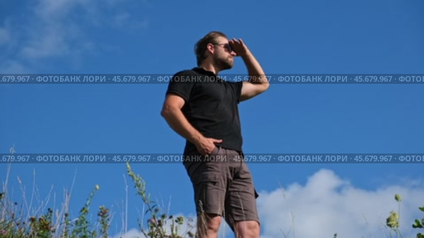 Handsome confident man standing with arms crossed among blue sky background. Male looking proud showing vision, ambition, success with arms folded. Bearded man wearing sunglasses, black polo t-shirt. Стоковое видео, видеограф Марина Демидюк / Фотобанк Лори