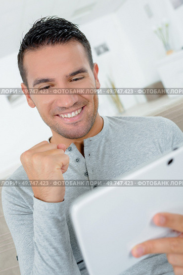 handsome euphoric winner watching a tablet in his living room. Стоковое фото, агентство Ingram Publishing / Фотобанк Лори