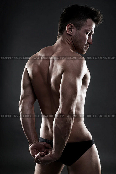 Handsome muscular bodybuilder posing on gray background. Low key studio shot. Стоковое фото, фотограф Станислав Тарко / Фотобанк Лори