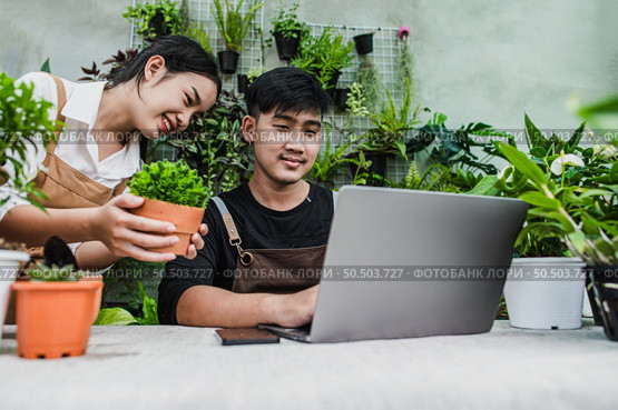 Happily gardener couple use laptop computer while online tutorial on potted plans in workshop together, vlogging or small business houseplant concept. Стоковое фото, агентство Ingram Publishing / Фотобанк Лори