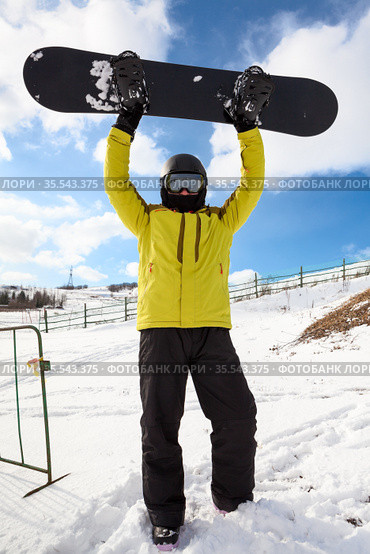 Happy Caucasian male snowboarder wearing helmet and glasses, full length portrait over blue sky in mountains rising up his board. Стоковое фото, фотограф Кекяляйнен Андрей / Фотобанк Лори