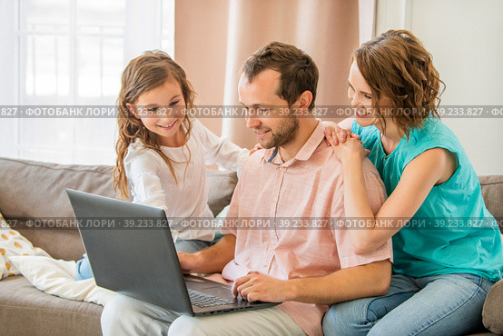 Happy family, mom, dad and daughter are sitting on couch and looking at laptop monitor together. Стоковое фото, фотограф Мария Мороз / Фотобанк Лори
