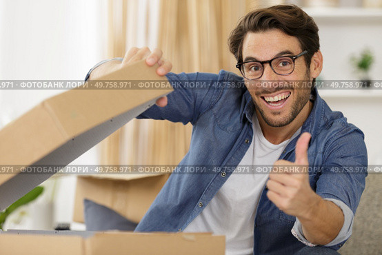 happy man opening parcel box at home showing thumb up. Редакционное фото, агентство Ingram Publishing / Фотобанк Лори