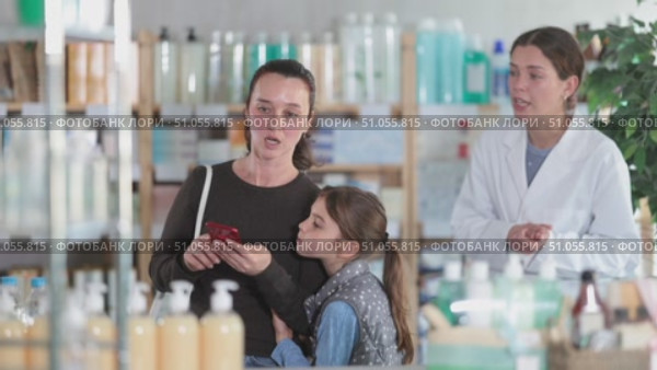 Happy mother with daughter scrolling phone while looking for something, pharmacist consulting her in drugstore. Стоковое видео, видеограф Яков Филимонов / Фотобанк Лори