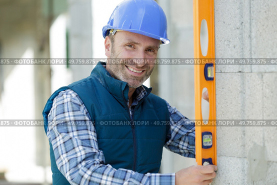 happy worker checks erected brick wall with level. Стоковое фото, агентство Ingram Publishing / Фотобанк Лори