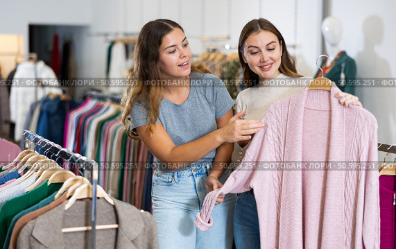 Happy young women testing fabrics of pink cardigan while shopping in a mall. Стоковое фото, фотограф Яков Филимонов / Фотобанк Лори