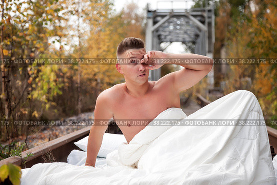 Homeless emotional young athletic beautiful Topless Caucasian man woke up in his bed on railway tracks. Concept of travel ban and inability to move. Stay at home. Copy space for site. Стоковое фото, фотограф Aleksandr Golubev / Фотобанк Лори