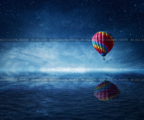 Hot air balloon flying over the a cold dark blue sea. Wonderful landscape with a starry night sky background and water reflection. Стоковое фото, агентство Ingram Publishing / Фотобанк Лори