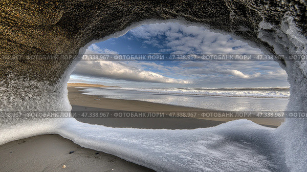 Icy coastal cave view: winter beach scene with clouds and ocean waves. Стоковое AI-изображение, AI-художник Olga Didraga / Фотобанк Лори