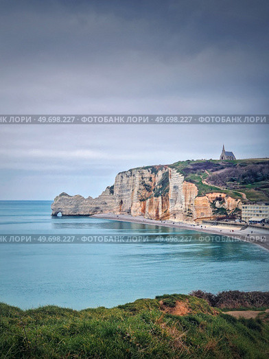 Idyllic view to Etretat coastline with the famous Notre-Dame de la Garde chapel on the Amont cliff. Shore washed by Atlantic ocean waters, Normandy, France. Стоковое фото, агентство Ingram Publishing / Фотобанк Лори