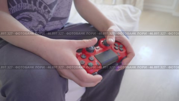Игровой процесс с красным геймпадом PlayStation вид сбоку. Ребёнок играет в видеоигру, держа в руках красный геймпад PlayStation. Редакционное видео, видеограф Анна Чижова / Фотобанк Лори