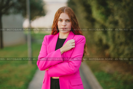 In an outdoor setting that showcases lush greenery and vibrant colors, a stylish young woman, dressed in a striking pink blazer, poses confidently, exuding an air of elegance and modern femininity. A Confident Young Woman Dressed in a Pink Blazer is Posing Outdoors with Style and Grace. Стоковое фото, агентство Ingram Publishing / Фотобанк Лори