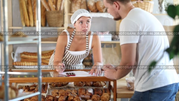 In bakery, male visitor and female salesperson work with paper documents and count using phone. Стоковое видео, видеограф Яков Филимонов / Фотобанк Лори