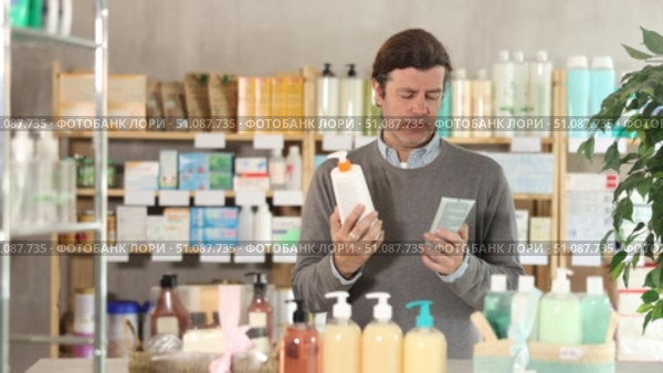 In drug store, man examine body lotion packaging, buy product. Стоковое видео, видеограф Яков Филимонов / Фотобанк Лори