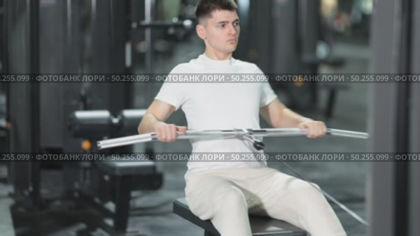 In gym, young man uses cable row machine to strengthen arm muscles. Стоковое видео, видеограф Яков Филимонов / Фотобанк Лори