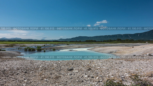 In the caldera of an extinct volcano there is a turquoise translucent lake from hot springs. There are sulphurous deposits on the rocky soil around. Mountains against the blue sky. Kamchatka. Uzon. Стоковое фото, фотограф Вера Ивановна Кубарева / Фотобанк Лори