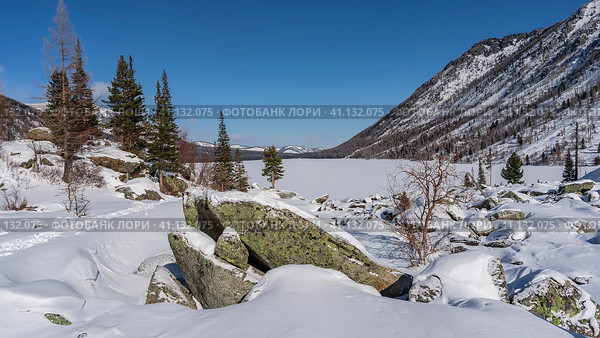 In the valley, under a layer of snow, there are picturesque boulders. A chain of footprints trampled through snowdrifts leads to a frozen lake with a snow-covered untouched surface. Altai. Стоковое фото, фотограф Вера Ивановна Кубарева / Фотобанк Лори