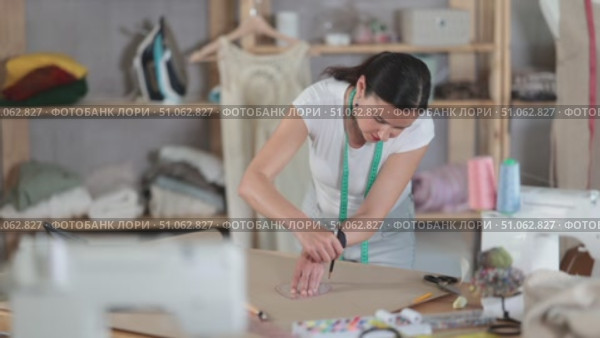 In workshop, woman designer draws diagram of future clothing product on paper. Creating dress pattern according to individual sizes, preparatory stage of work in sewing production. Стоковое видео, видеограф Яков Филимонов / Фотобанк Лори