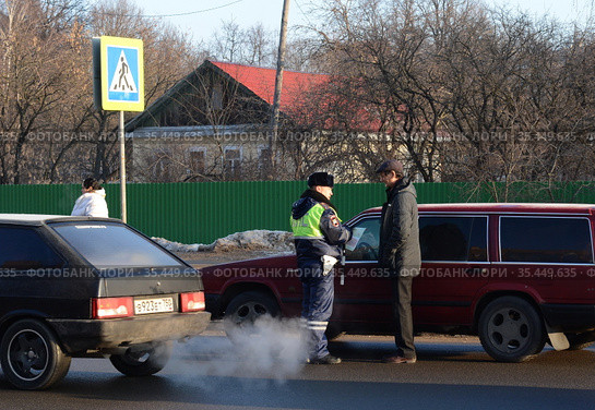 Инспектор дорожно-патрульной службы полиции проверяет документы водителя остановленного автомобиля (2016 год). Редакционное фото, фотограф Free Wind / Фотобанк Лори