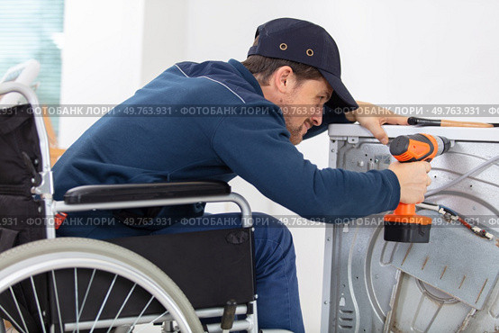 invalid working man plumber repairs a washing machine in laundry. Стоковое фото, агентство Ingram Publishing / Фотобанк Лори
