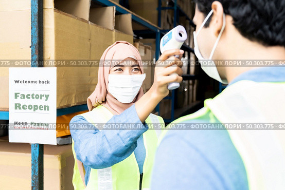 Islam asian warehouse worker take temperature to worker before getting in factory after reopening after city lockdown from COVID-19 coronavirus pandemic in warehouse distribution center environment. Стоковое фото, агентство Ingram Publishing / Фотобанк Лори