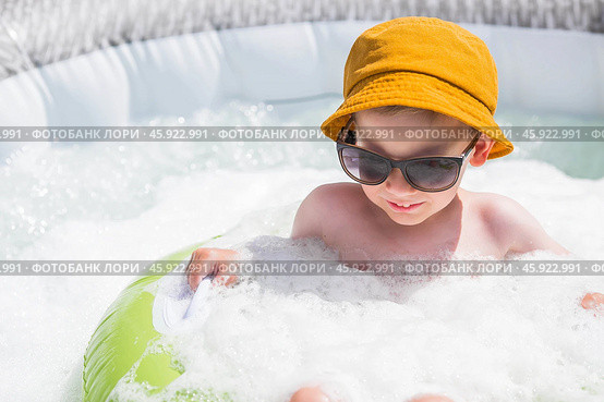It's a hot day. A cute boy in sunglasses and a panama hat swims on a circle in a foam pool. The concept of summer holidays with children. Стоковое фото, фотограф Photojuli / Фотобанк Лори