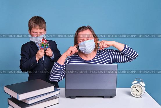 Junior boy in a school uniform prevents his mother from working remotely on a laptop. Problems when working from home during the coronavirus epidemic. Стоковое фото, фотограф Андрей Журавлев / Фотобанк Лори