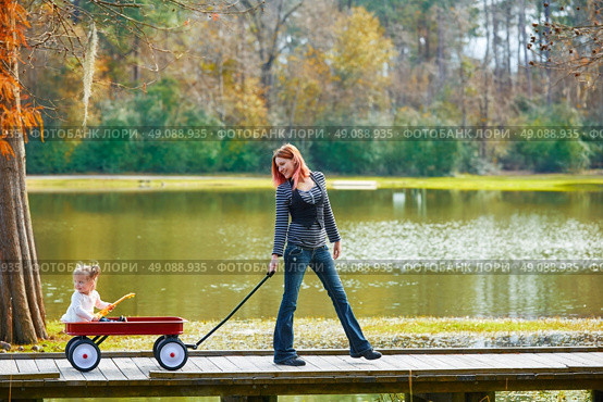 Kid girl and mother walking in the park lake with pull cart. Стоковое фото, агентство Ingram Publishing / Фотобанк Лори