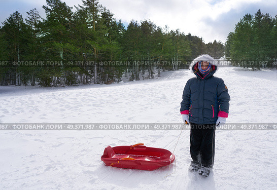 Kid girl with sled in a snowed mountain slope in a cold day. Стоковое фото, агентство Ingram Publishing / Фотобанк Лори
