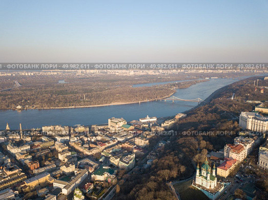 Kiev, Ukraine - April 7, 2018: Panoramic view of the district hem and Andreevskaya church. The Dnieper River is a pedestrian bridge and the Trukhanov island is a sunny day. Photo from the drone. Kiev, Ukraine - April 7, 2018: Panoramic view of the Dnieper River pedestrian bridge, Trukhanov Island and Andreevskaya church . Редакционное фото, агентство Ingram Publishing / Фотобанк Лори