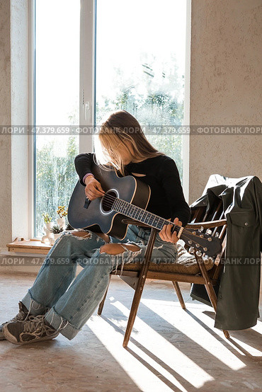 Learning to play the guitar. Music. A talented girl musician sits alone and plays songs on the guitar. The girl plays a calm melody on a musical instrument. Стоковое фото, фотограф Photojuli / Фотобанк Лори