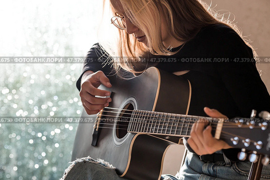 Learning to play the guitar. Music. A talented girl musician sits alone and plays songs on the guitar. The girl plays a calm melody on a musical instrument. Стоковое фото, фотограф Photojuli / Фотобанк Лори