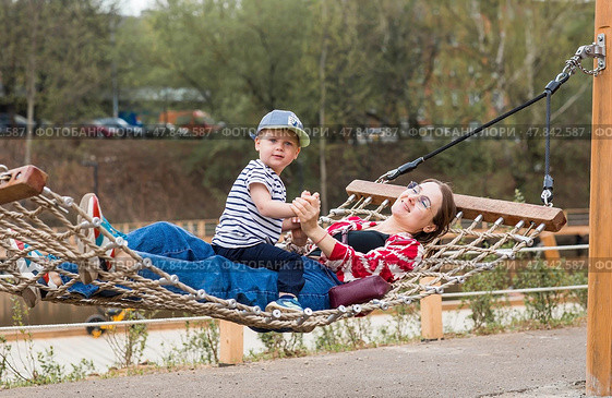 Lifestyle. A cute little boy and his mom are lying in a hammock on a modern outdoor playground. The concept of family privacy and entertainment. Стоковое фото, фотограф Photojuli / Фотобанк Лори