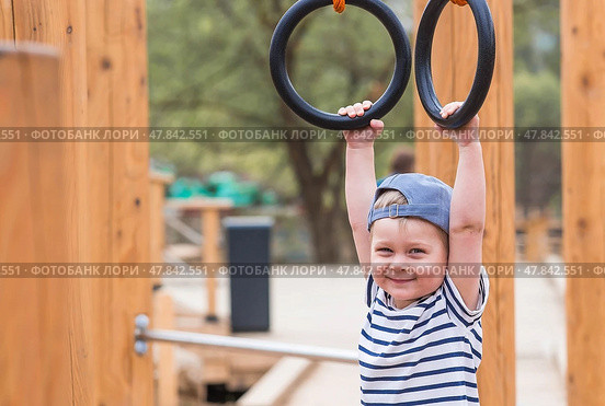 Lifestyle. A cute little boy is hanging on rings on a sports field in the fresh air. The concept of children's sports and physical development. Стоковое фото, фотограф Photojuli / Фотобанк Лори
