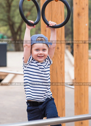 Lifestyle. A cute little boy is hanging on rings on a sports field in the fresh air. The concept of children's sports and physical development. Стоковое фото, фотограф Photojuli / Фотобанк Лори