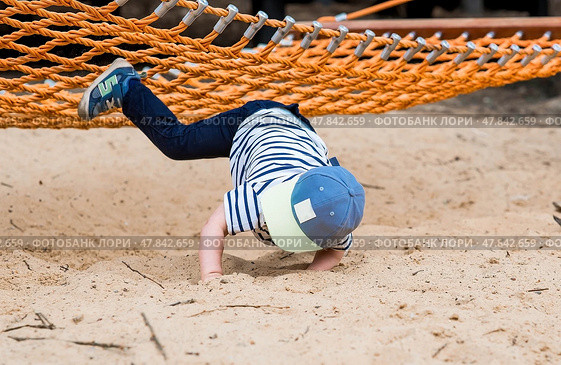 Lifestyle. Child safety. A cute little boy fell from a swing, hammock on a modern playground. The concept of caring for young children. Стоковое фото, фотограф Photojuli / Фотобанк Лори