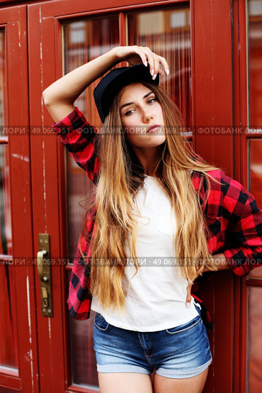 Lifestyle portrait of fashionable blonde girl with ombre hair wearing a rock red shirt, black cap, white t-shirt and denim shorts having fun outdoors in the city. Swag style. Стоковое фото, агентство Ingram Publishing / Фотобанк Лори