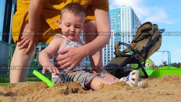 Little baby learns to play with sand in a children's sandbox under the control of a mother woman. Kid aged one year. Стоковое видео, видеограф Андрей Журавлев / Фотобанк Лори