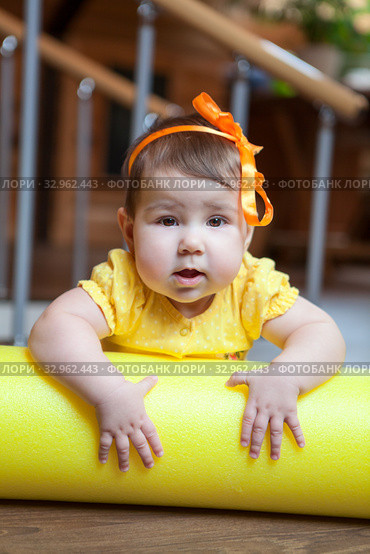Little girl portrait, baby lying on yellow foam roller in domestic gym, looking at camera. Стоковое фото, фотограф Кекяляйнен Андрей / Фотобанк Лори
