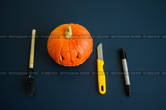 Little pumpkin with spiteful grimass, paper knife, pen, trowel over black background. Halloween concept, flat lay, top view. The process of making jack-o-lantern. flat lay. Стоковое фото, фотограф Михаил Решетников / Фотобанк Лори