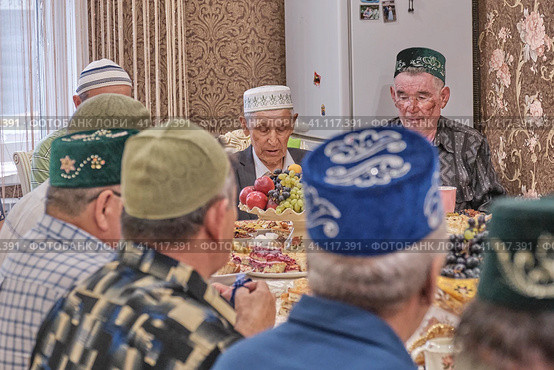 Local residents of Siberian village celebrate Muslim holiday Kurban Bayram at their home table. Mullah saying prayer. Eid al-Adha (2021 год). Редакционное фото, фотограф Ирина Кононова / Фотобанк Лори