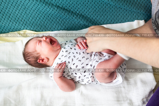 Loud crying baby with abdominal pain laying on bedsheet, human hands touching belly and calming. Стоковое фото, фотограф Кекяляйнен Андрей / Фотобанк Лори