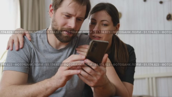 Loving mature couple using mobile phone. Husband and wife hugging, holding hands and looking at the smartphone screen. Man and woman share content on social media app. Young people watch the cellphone. Стоковое видео, видеограф Марина Демидюк / Фотобанк Лори