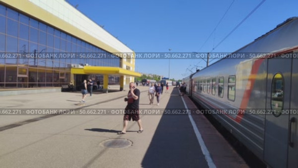 Люди прогуливаются по перрону вдоль железнодорожных вагонов. Пассажиры ходят по платформе во время остановки поезда. Современная железнодорожная станция. Россия, Ярославль, 22 мая 2025. People walking along platform along railway cars. Passengers walk on platform during train stop. Modern railway station. Russia, Yaroslavl, May 22, 2025. Редакционное видео, видеограф Ирина / Фотобанк Лори