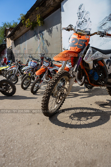 Magnitogorsk, Russian Federation - August 23, 2025: Enduro motorcycles lined up against a textured wall, showcasing vibrant colors and rugged designs, ready for competition and adventure. Редакционное фото, фотограф Ирина Ручушкина / Фотобанк Лори