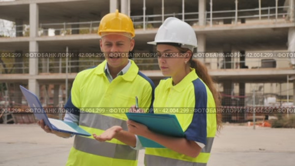 Male and female egineers standing in construction site, planning project of new multistory building and checking documentation. Стоковое видео, видеограф Яков Филимонов / Фотобанк Лори