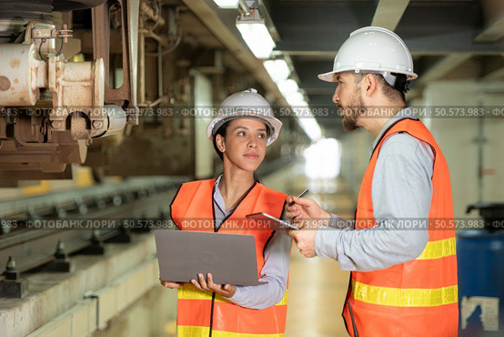 Male and female engineers work together in an electric repair station. Inspecting the undercarriage of electric train that are being repaired at the garage. Стоковое фото, агентство Ingram Publishing / Фотобанк Лори
